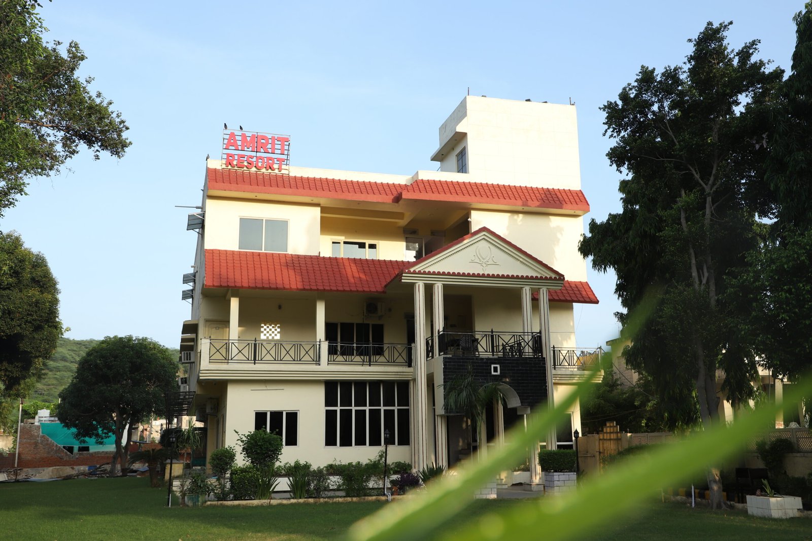 A resort sign is prominently displayed, surrounded by lush tropical plants and palm trees. The sky is blue with scattered clouds, creating a serene atmosphere.